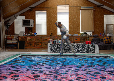 View of JonOne's creating a large painting laying on the ground.